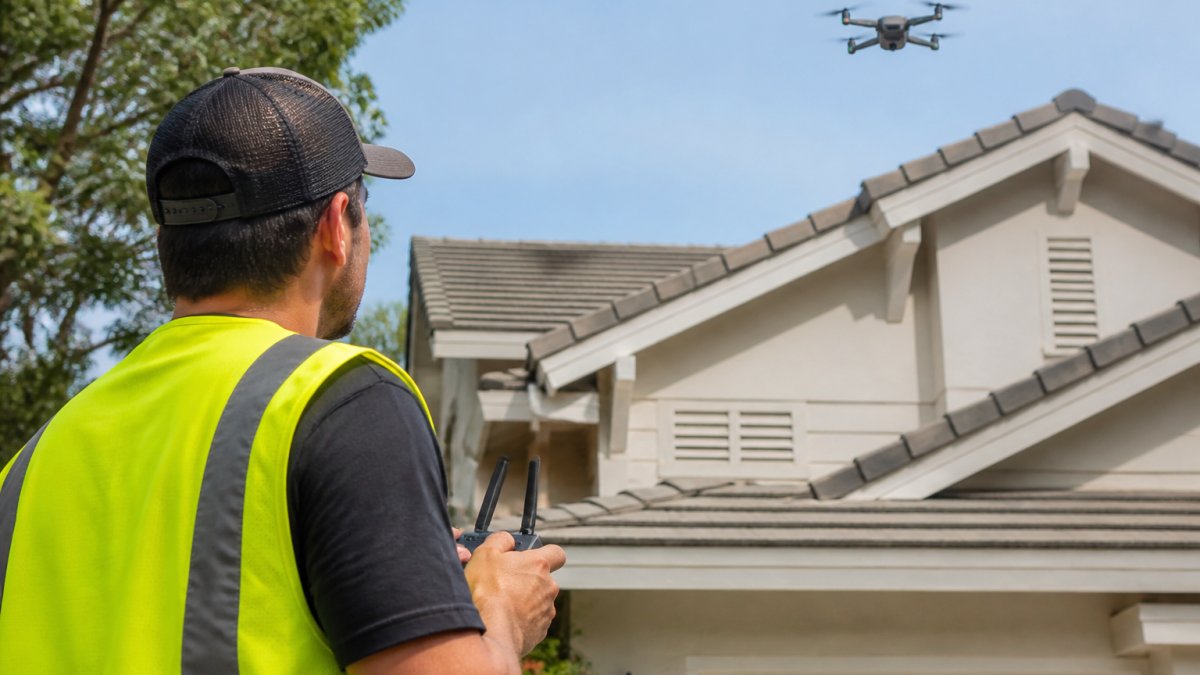 Drone operator using a remote to capture footage for a drone roof inspection cost assessment