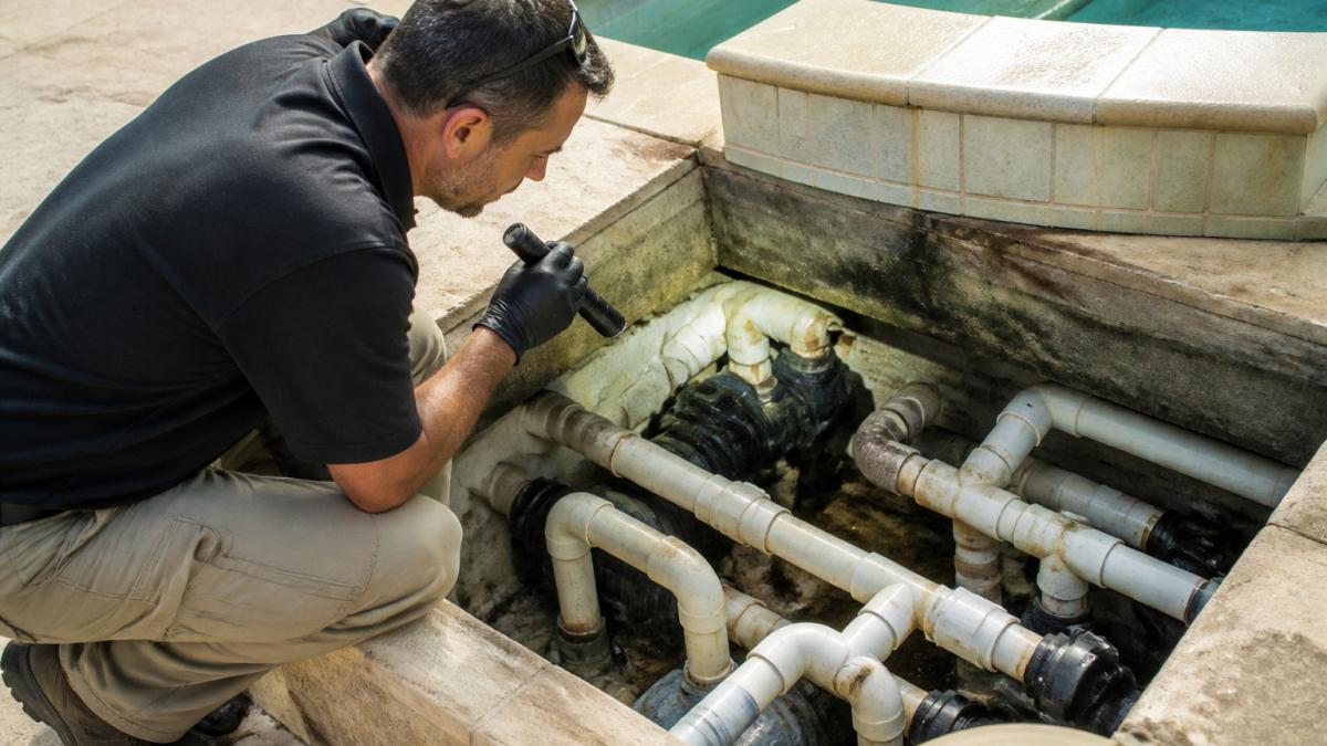 Inspector using tools to check pool plumbing for leaks during a pool and plumbing inspection checklist assessment
